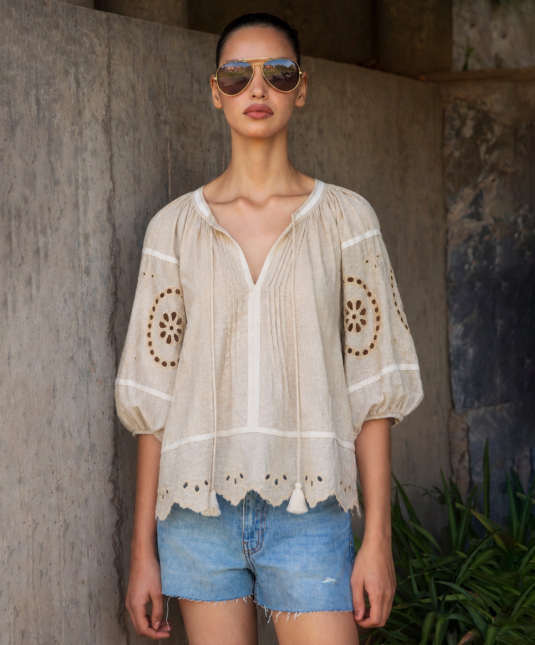 Woman wearing a natural linen embroidered blouse and blue denim shorts standing in a rustic setting.