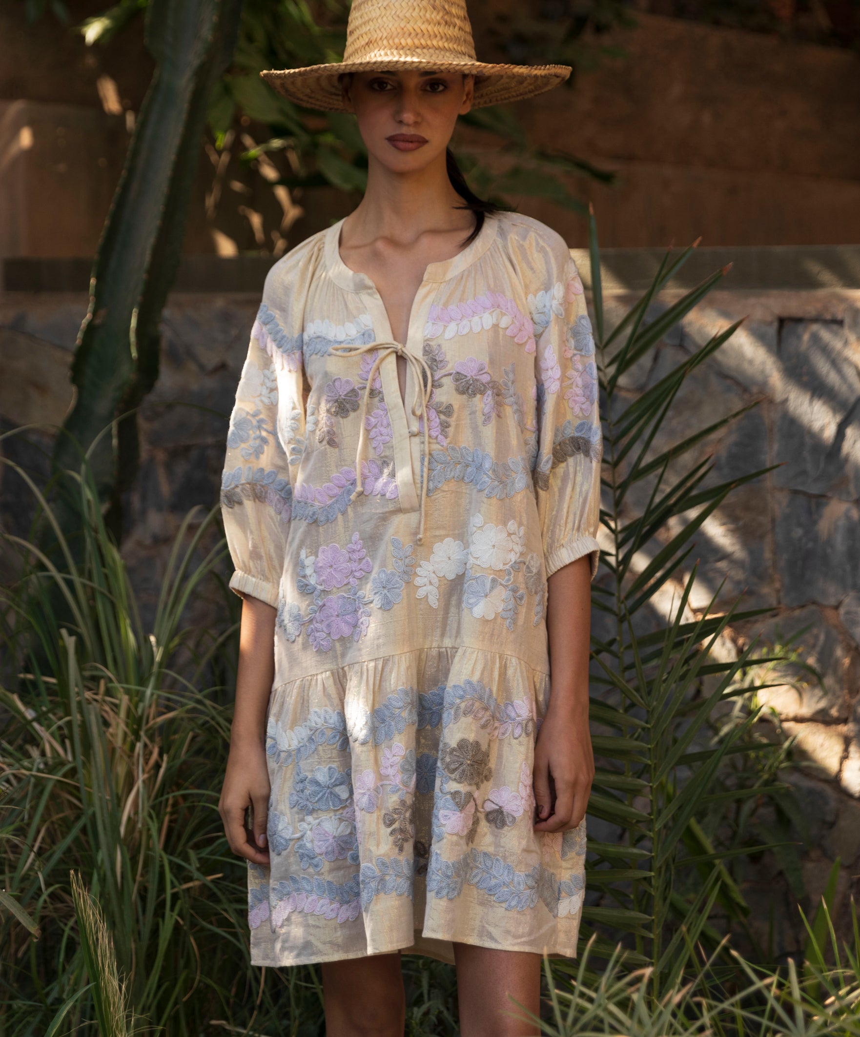Woman wearing a floral embroidered gold Oleander dress and straw hat in a tropical garden