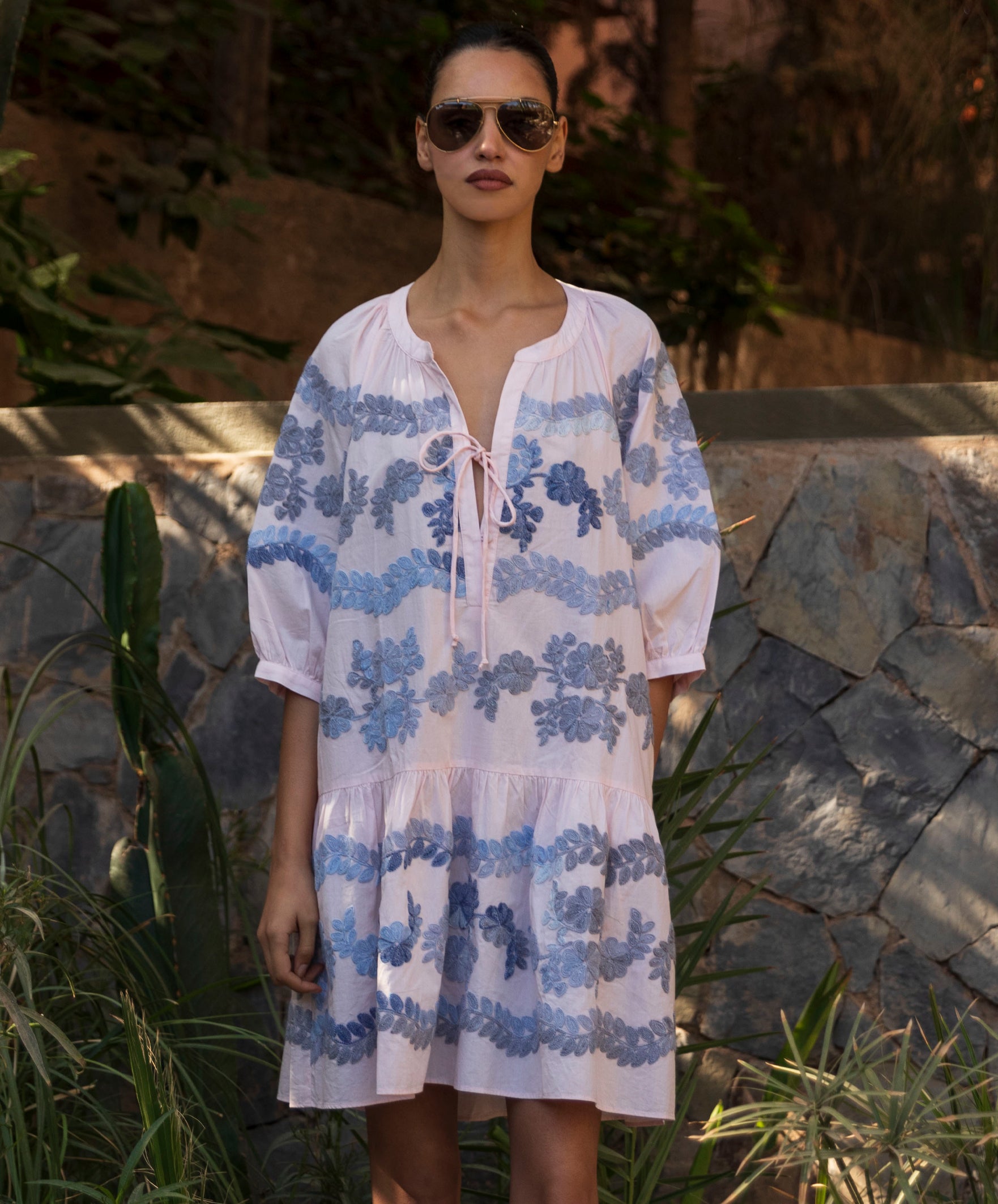 Woman wearing a light pink Oleander dress with blue floral embroidery pattern.