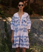 Woman wearing a light pink Oleander dress with blue floral embroidery pattern.