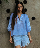 A model is wearing a Rose and Rose Oval top in blue slub with white appliqué decoration.