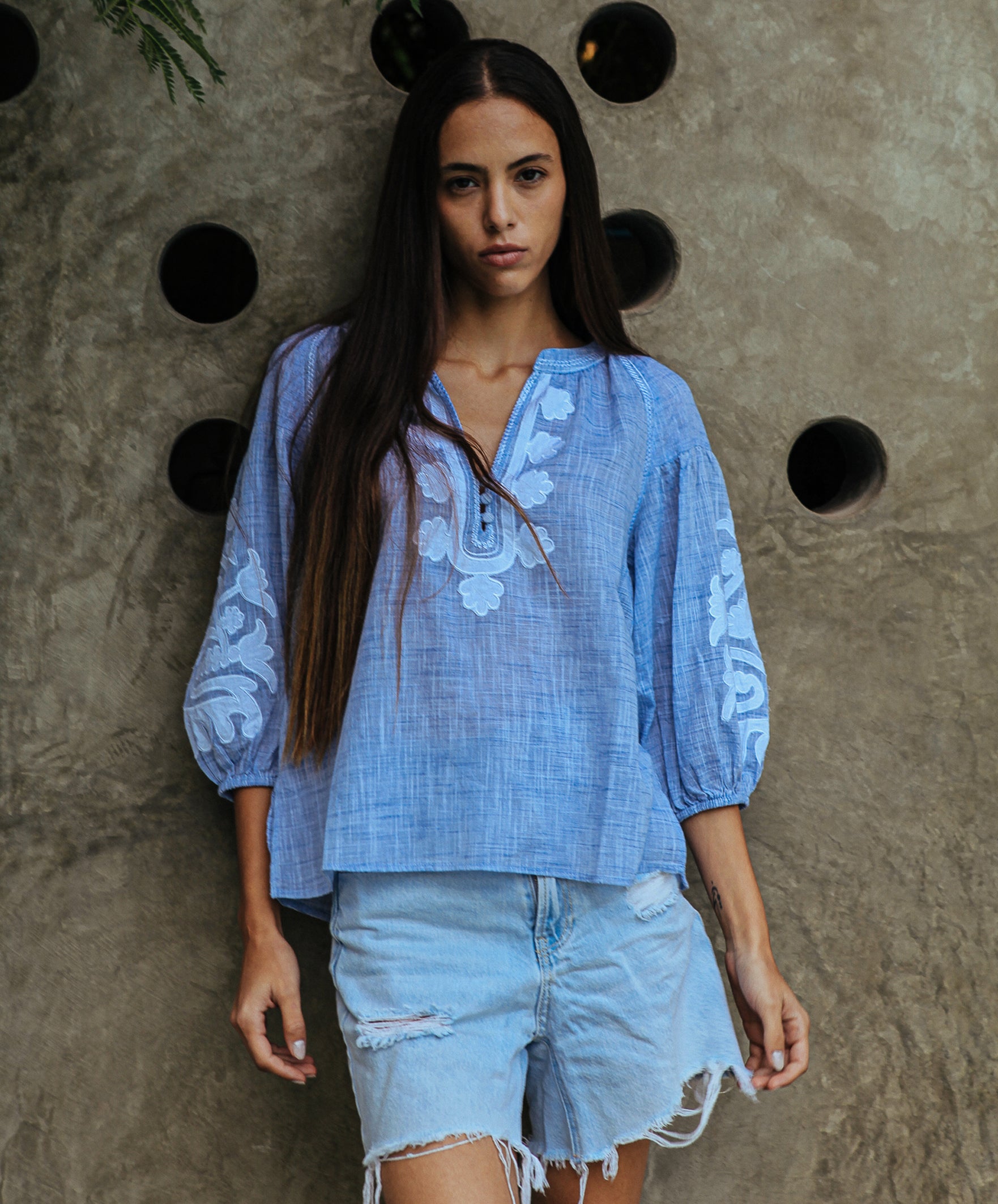 A model is wearing a Rose and Rose Oval top in blue slub with white appliqué decoration.