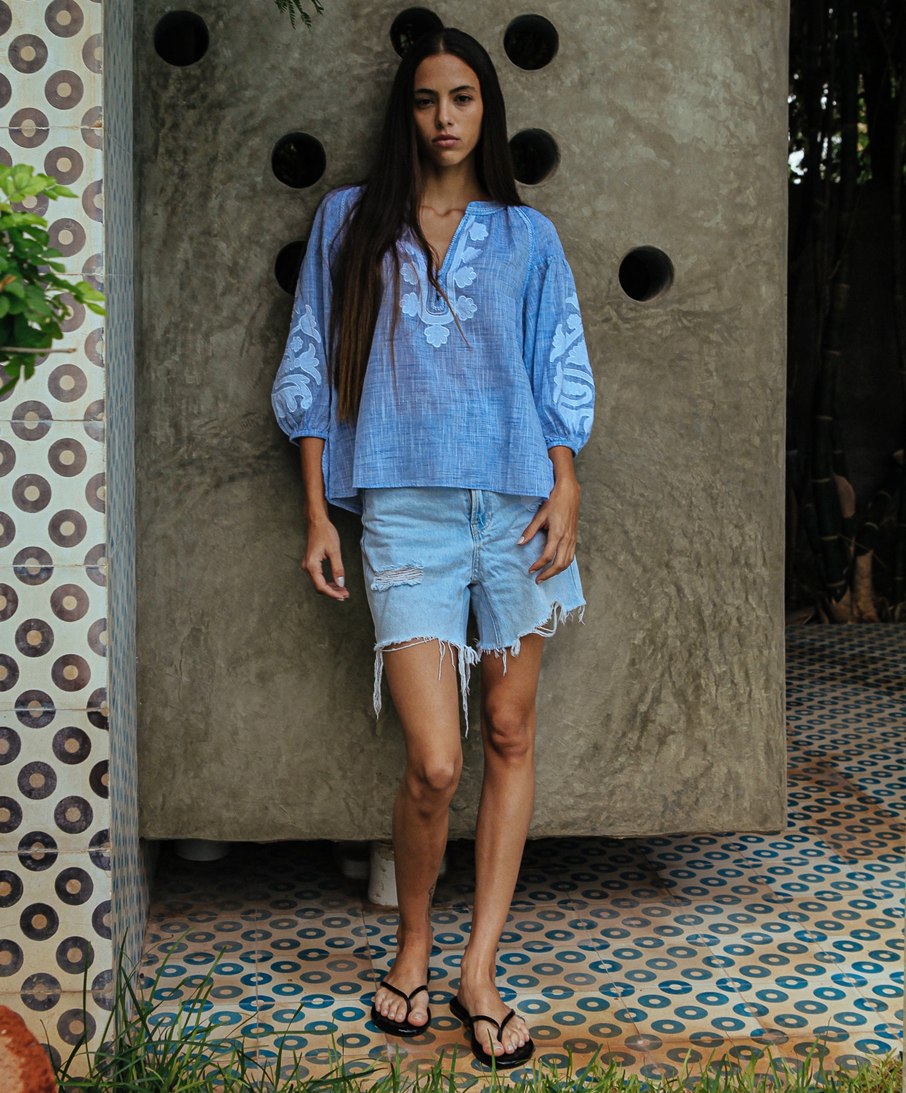 A model is wearing a Rose and Rose Oval top in blue slub with white appliqué decoration.