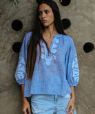 A model is wearing a Rose and Rose Oval top in blue slub with white appliqué decoration.