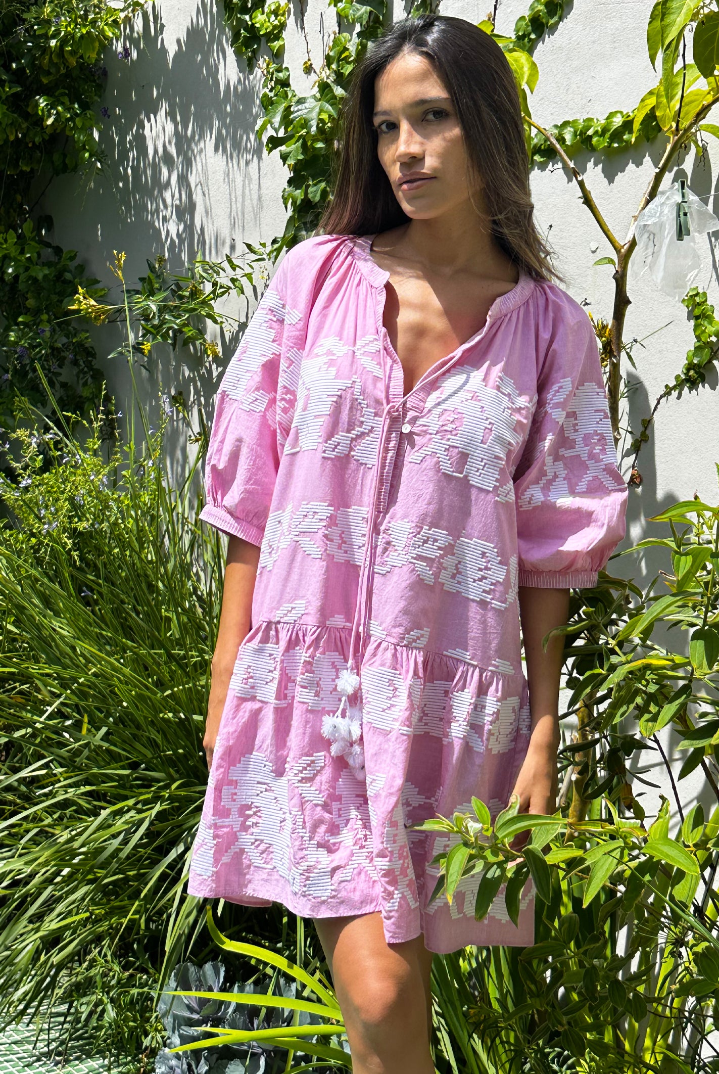 A model stood in a garden wearing a Rose and Rose pale pink Palermo embroidered dress. 
