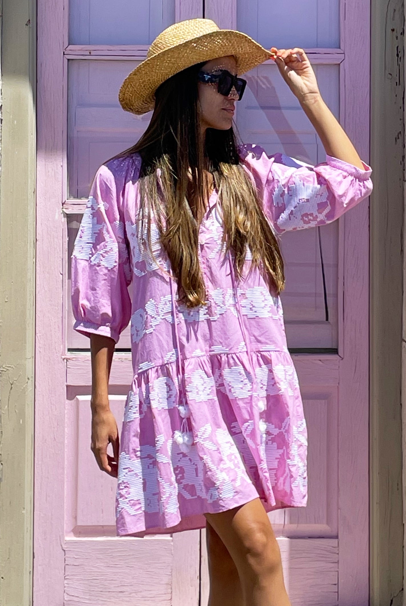 A model wearing sunglasses and a cowboy hat stood in front of a pink door wearing a Rose and Rose pale pink Palermo embroidered dress. 