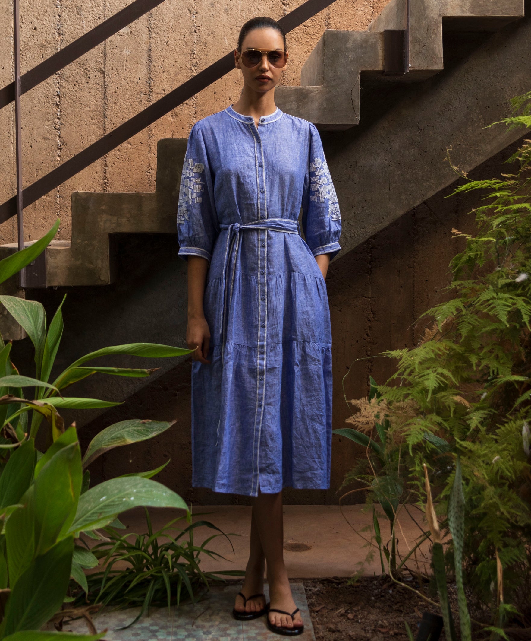 Woman in a blue chambray dress standing on a staircase with plants around