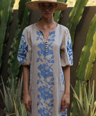 Close up of a woman wearing a natural Rose dress with blue embroidery and decoration, standing among cacti.