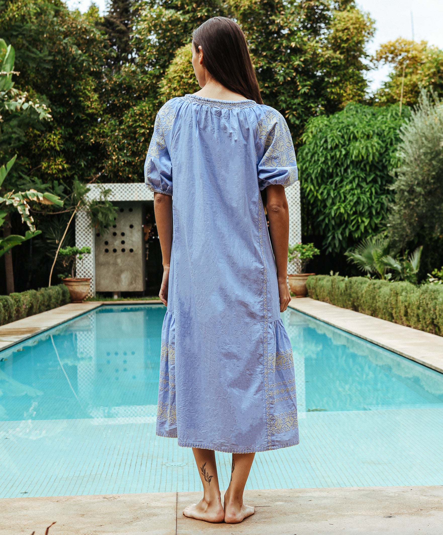 Black view of a model wearing a Rose and Rose embroidered Royal Oak dress in blue cotton.