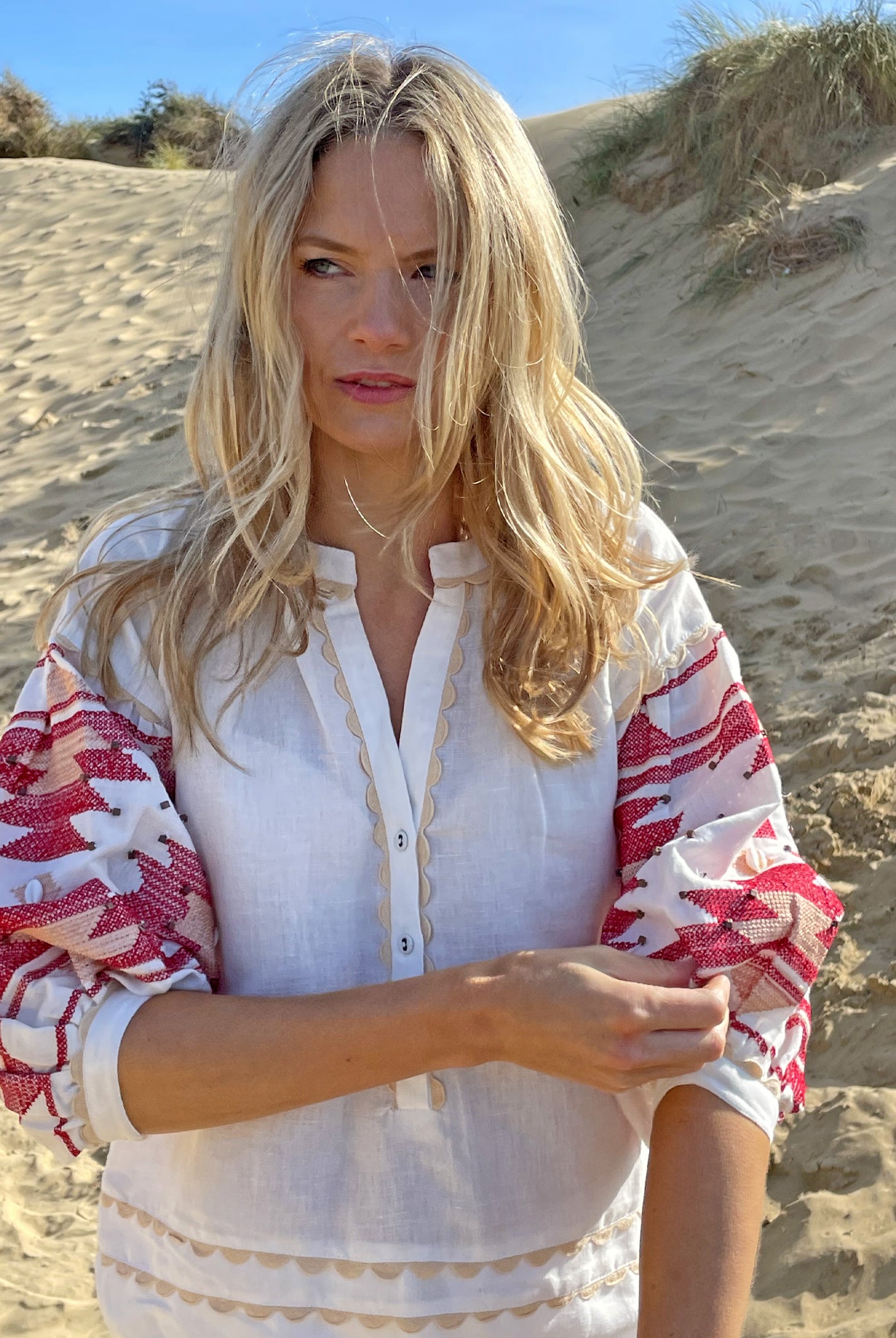 A model on a beach wearing the Rose and Rose white San Marino linen top with Navajo embroidery. 