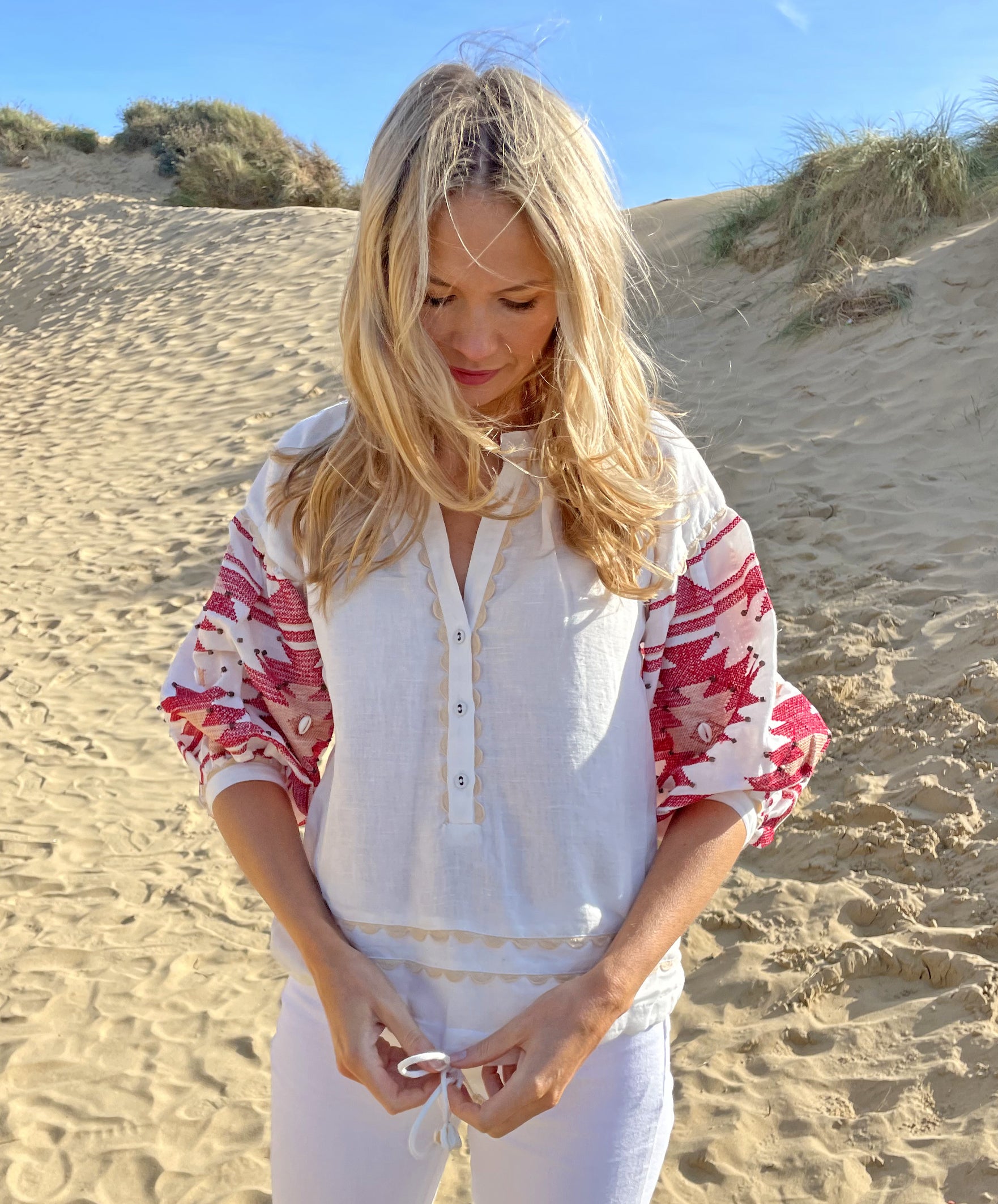 A model on a beach wearing the Rose and Rose white San Marino linen top with Navajo embroidery. 