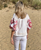 Back view of a model on a beach wearing the Rose and Rose white San Marino linen top with Navajo embroidery. 
