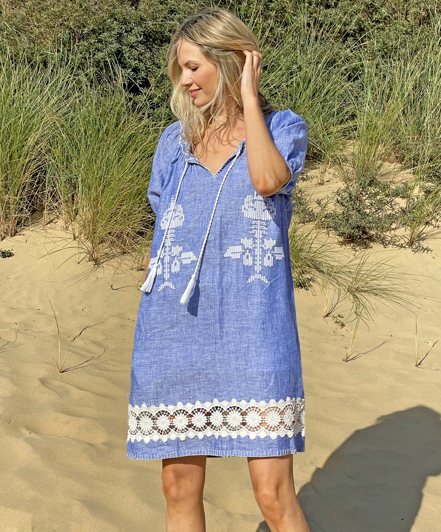 A model on a beach wearing the Rose and Rose Siracusa embroidered blue linen dress.
