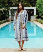 A model stood in  front of a swimming pool wearing a Rose and Rose Temple striped dress with embroidery and sequin decoration.