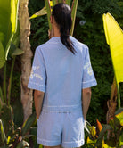 Back view of a woman wearing a blue striped shirt with matching shorts in a garden setting
