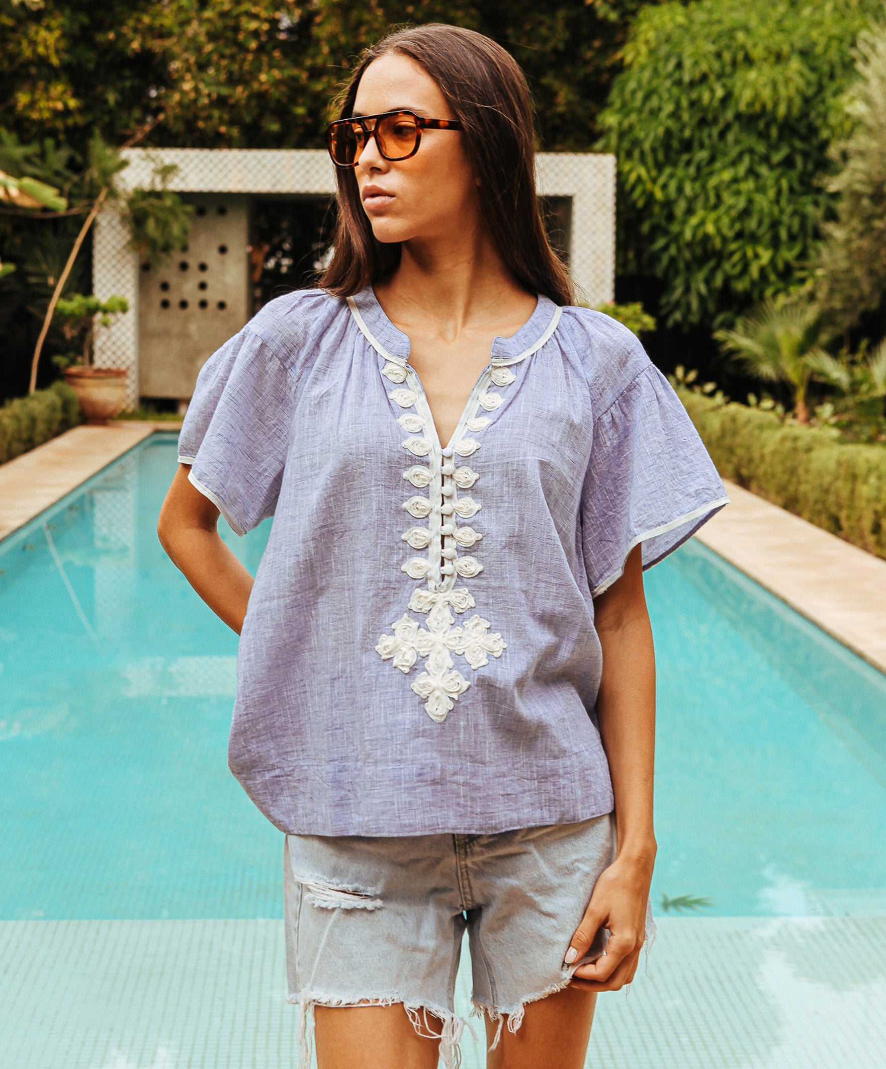 A model wearing a Rose and Rose Upminster blue top with white passementerie decoration. 