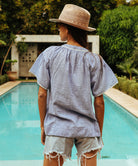 A back view of a model wearing a Rose and Rose Upminster blue top with white passementerie decoration. 