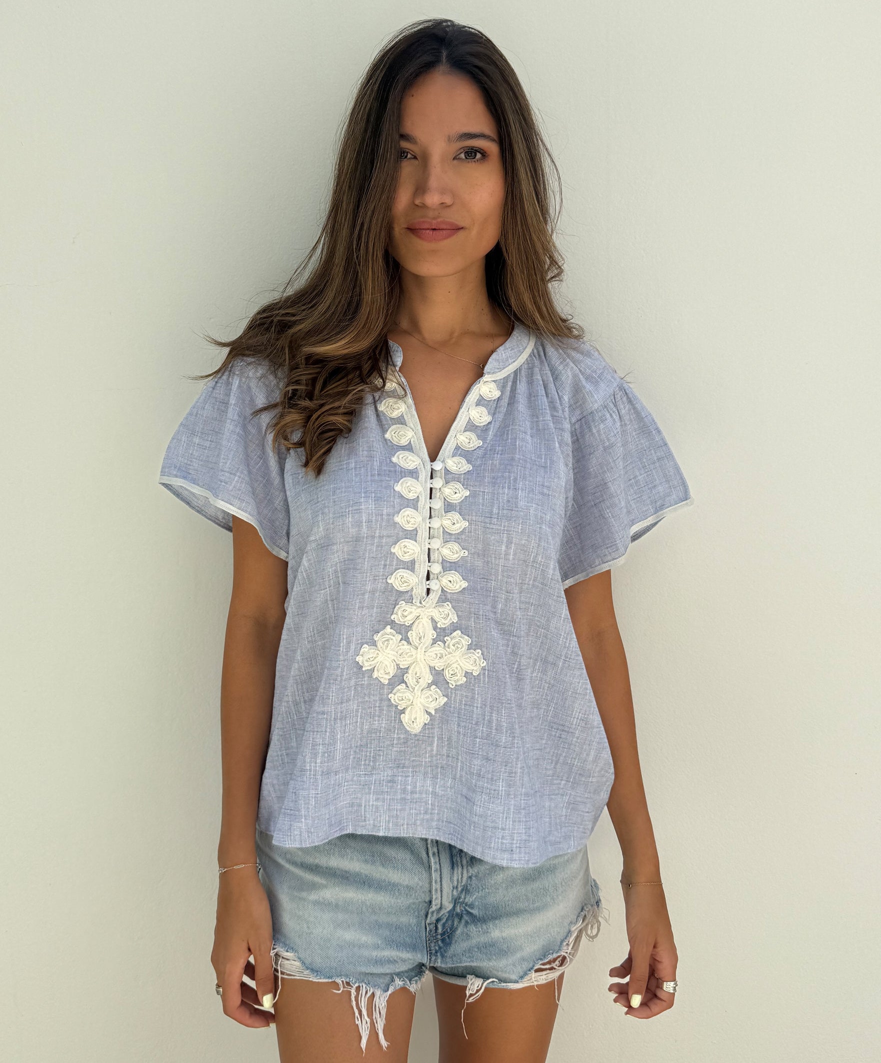 A model wearing a Rose and Rose Upminster blue top with white passementerie decoration. 