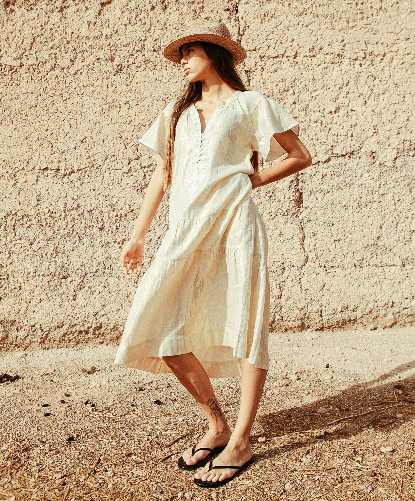 A model wearing a Rose and Rose Uxbridge gold dress with white passementerie decoration. 