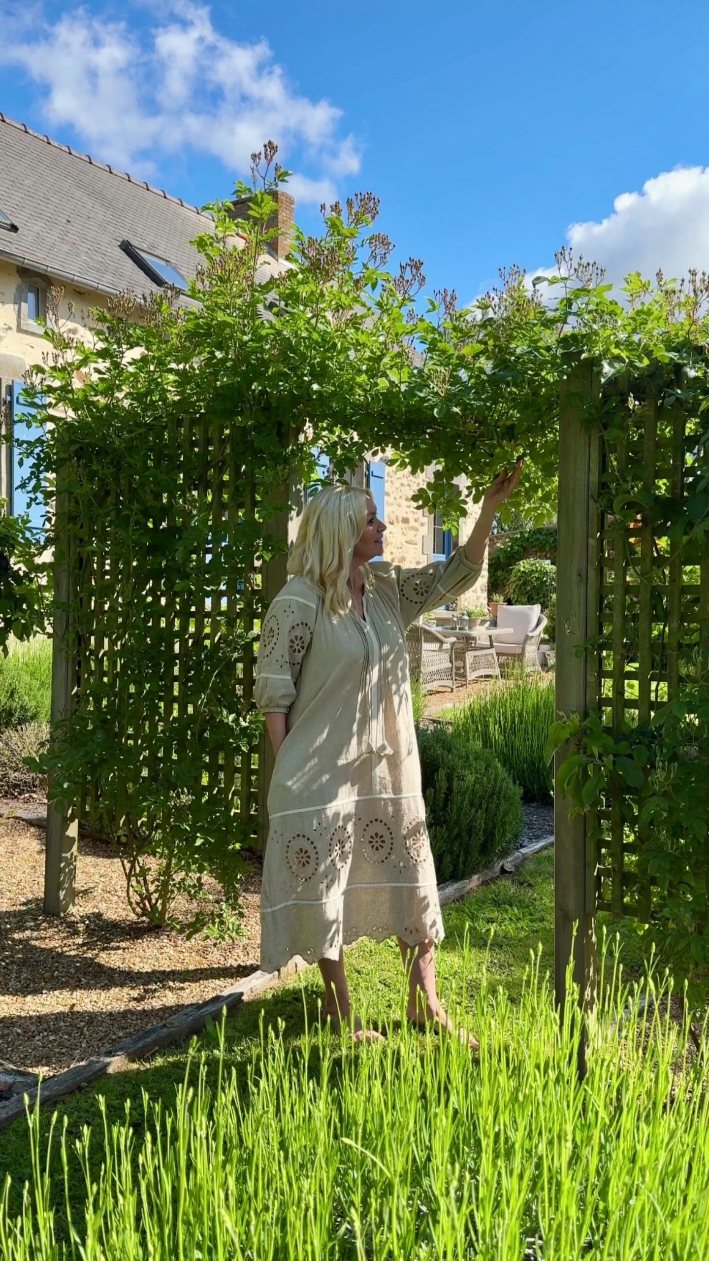 Influencer @shutters_and_stone wearing the Magnolia natural embroidered dress walking around her garden. 