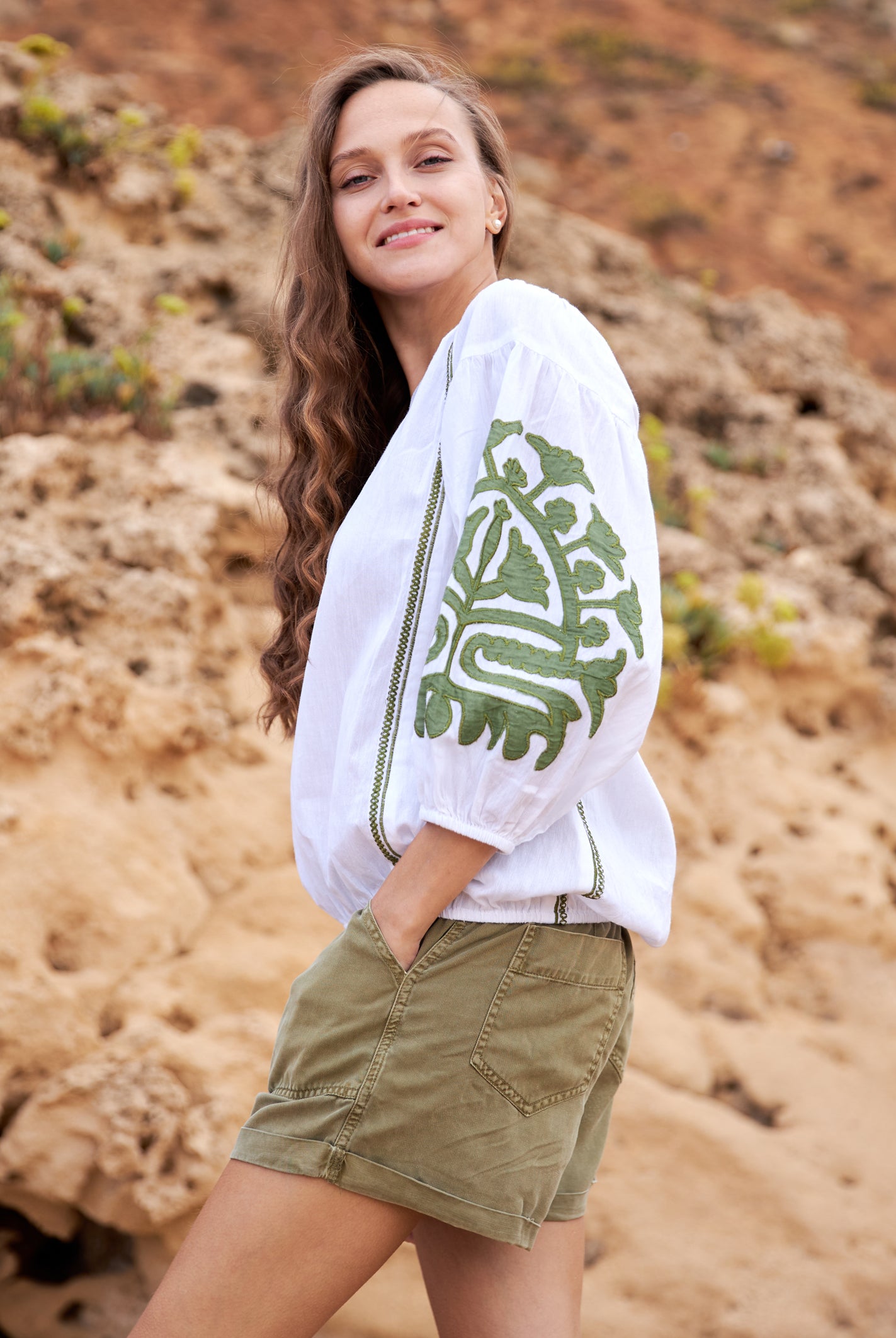 Close up of beautiful long brown haired model wearing a premium white cotton top with olive green appliqué motifs, and olive shorts.